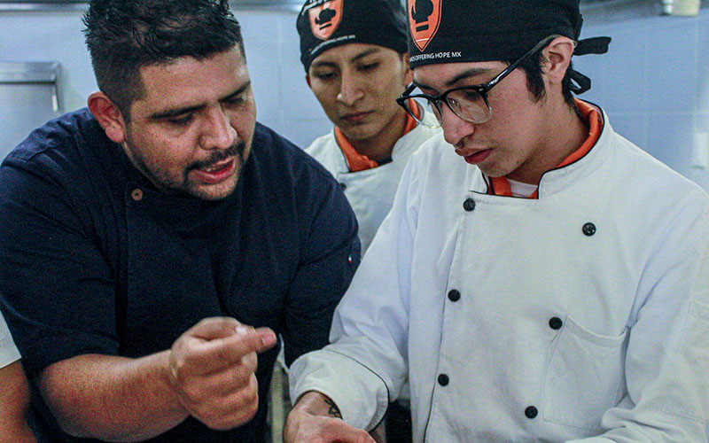 Two students chefs work with a visiting chef.